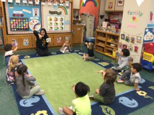 Preschool students and a teacher sitting on a carpet engaging in a lesson