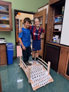 Two boys standing on a wooden bridge that is being built by middle school students