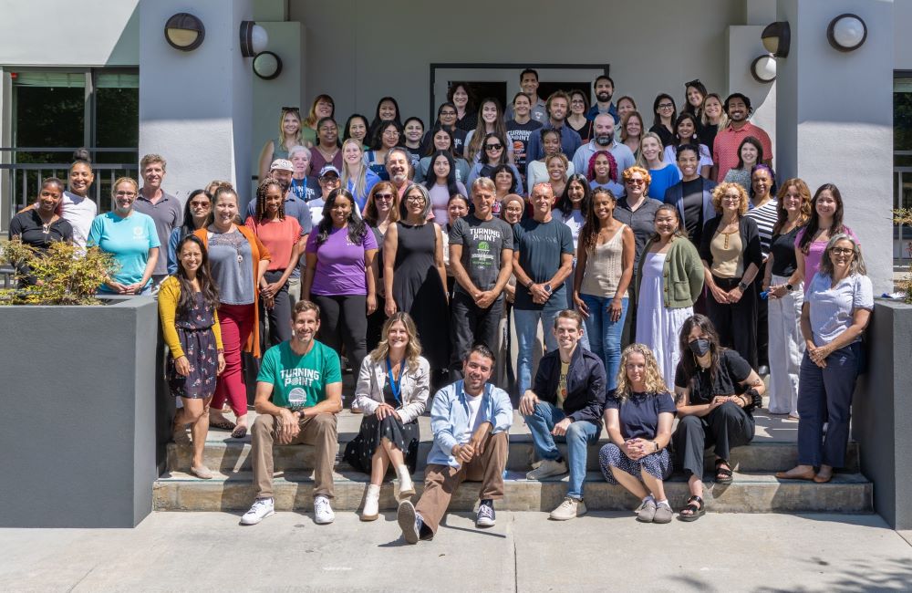 A group of approximately 50 Turning Point School faculty and staff members positioned on the steps of the school, smiling into the camera.